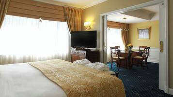 A hotel room with a large bed, a television, a desk with chairs, and a dining area.