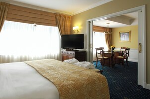 Habitación de hotel con una cama grande, televisión, escritorio con sillas y un comedor.
