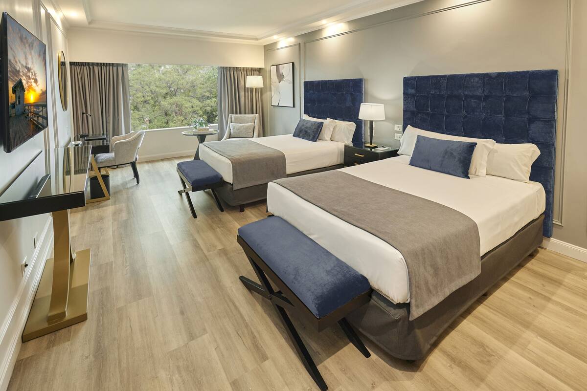 Een hotelkamer met twee bedden, een bureau, een stoel en uitzicht op de omgeving.