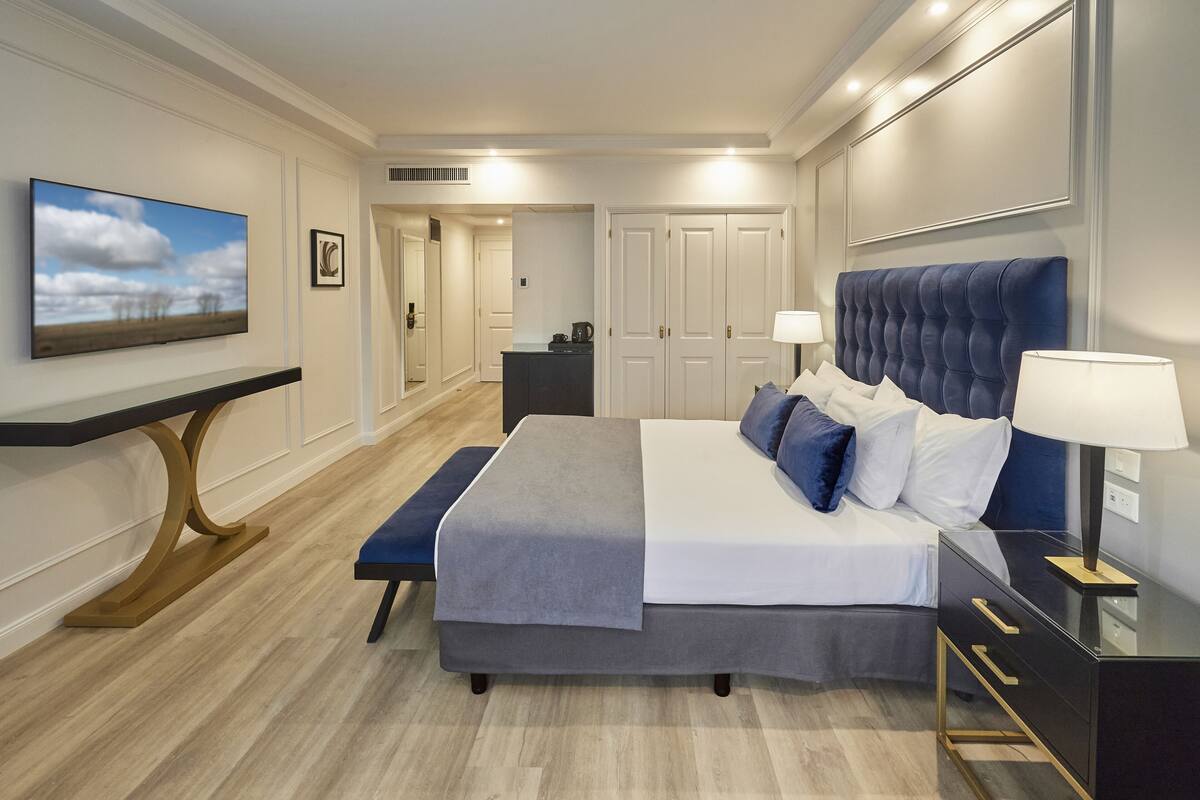Een moderne slaapkamer met een groot bed, nachtkastjes, een bureau en een televisie aan de muur.