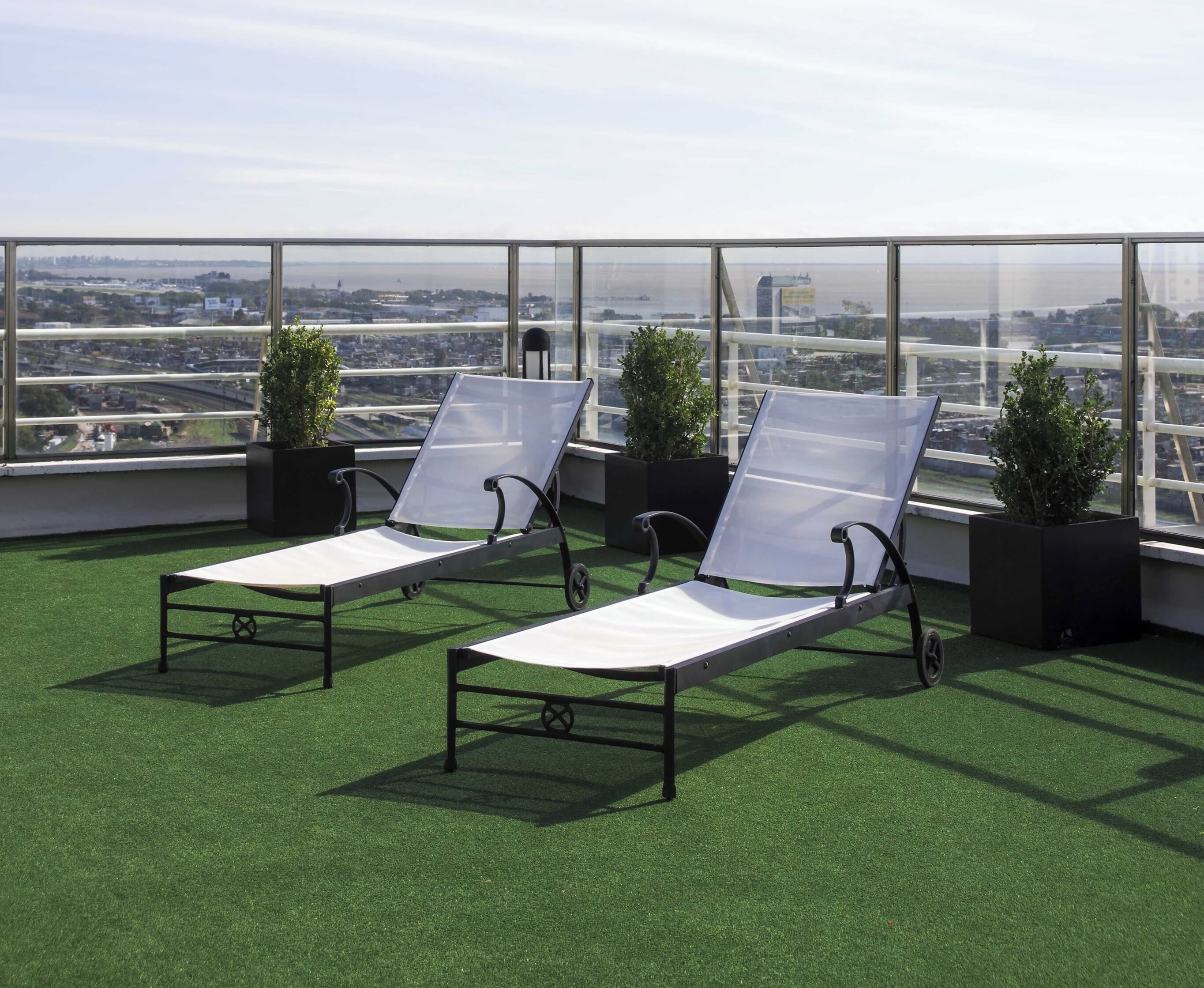Two lounge chairs on artificial grass with a city view through large windows.