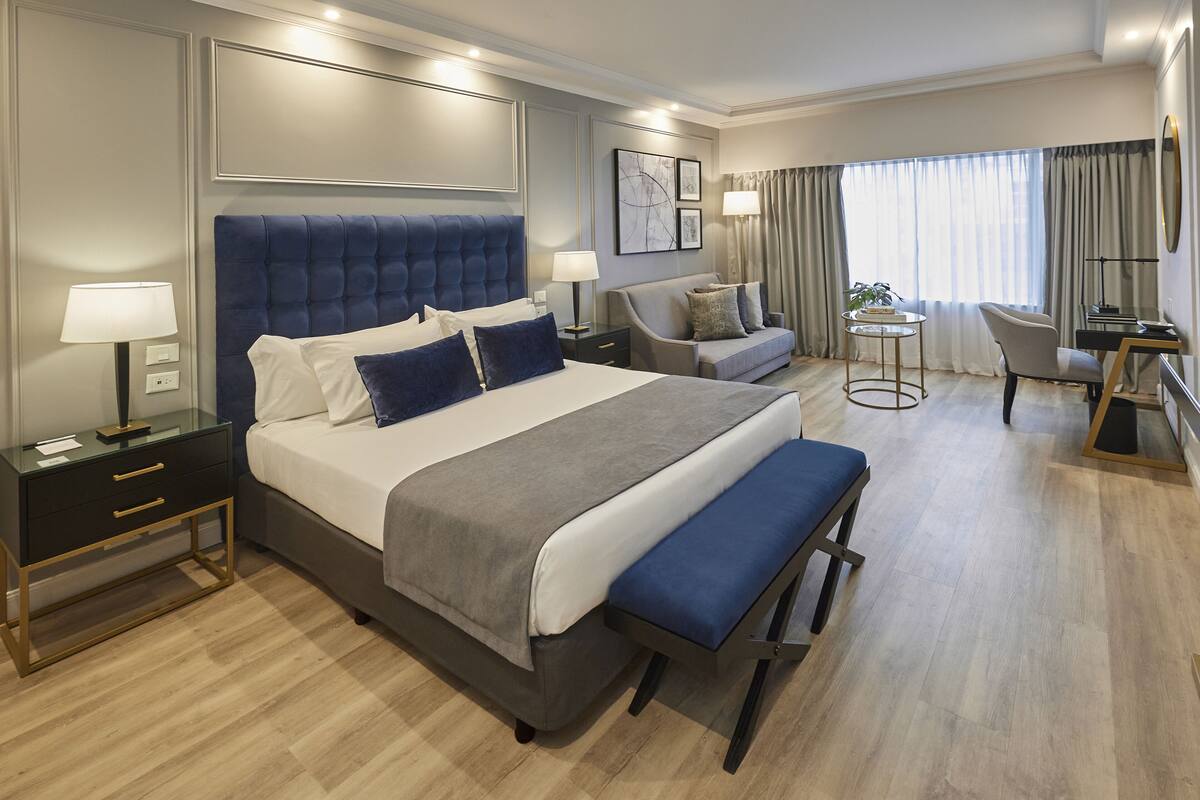 Een moderne hotelkamer met een groot bed, nachtkastjes, een bureau, een stoel en een bank.