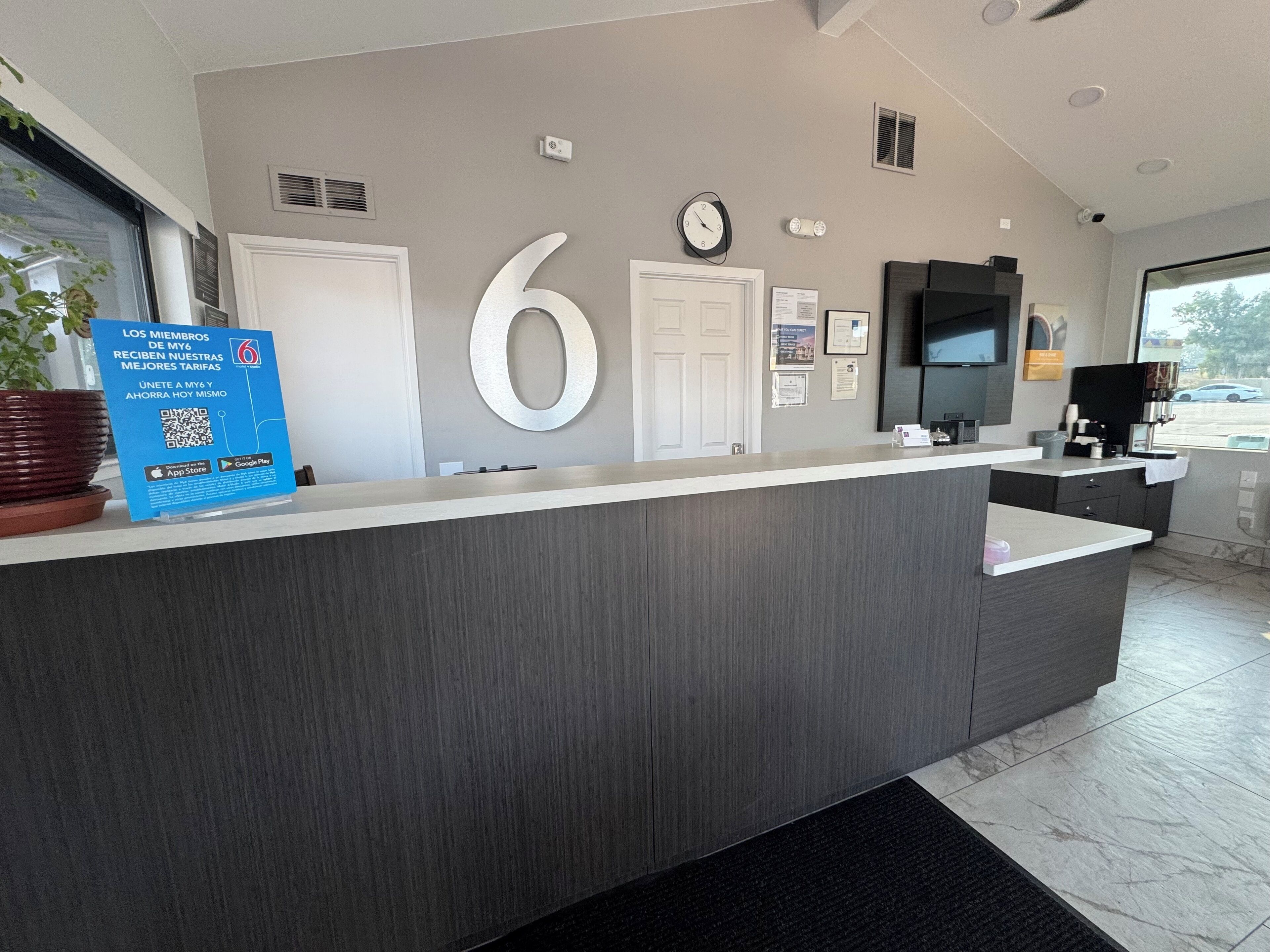Un comptoir d’accueil moderne, avec un grand chiffre « 6 » affiché sur le mur, une horloge et un panneau avec des codes QR.