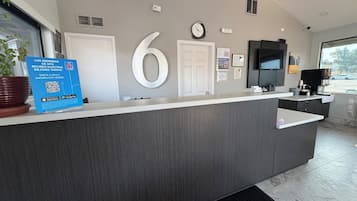 Un comptoir d’accueil moderne, avec un grand chiffre « 6 » affiché sur le mur, une horloge et un panneau avec des codes QR.