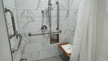 Un baño moderno con ducha, barras de apoyo, un lavamanos pequeño y un inodoro.