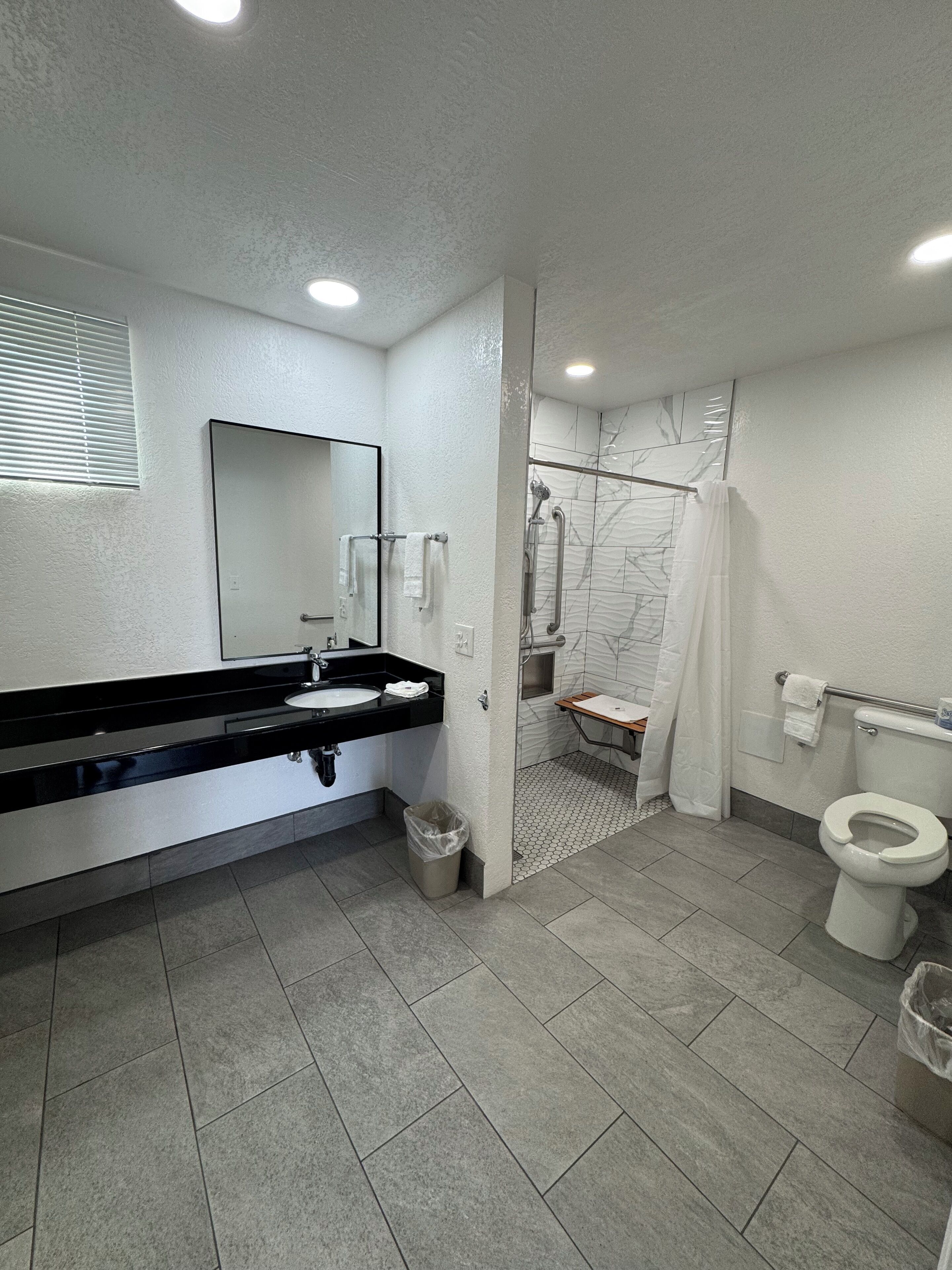 Un baño moderno con un lavamanos negro, inodoro blanco y zona de ducha con mampara de vidrio.