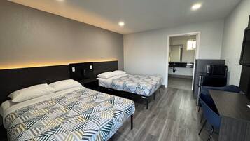 A hotel room with two beds, a desk, a TV, and a bathroom visible in the background.