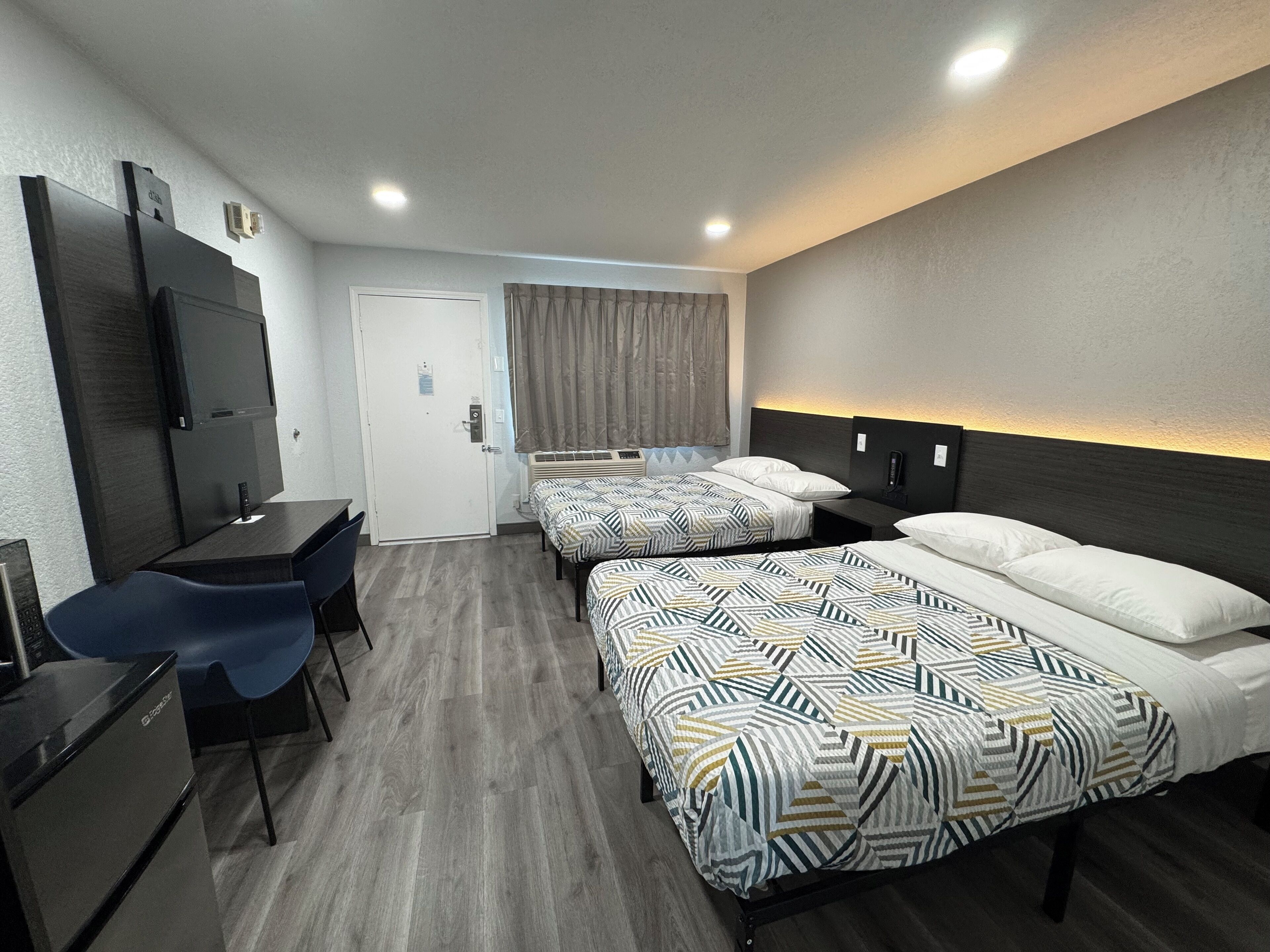 A hotel room with two beds, a desk, a chair, and a television.