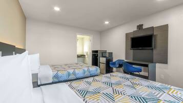 A hotel room with two beds, a desk, a chair, a TV, and a kitchenette.