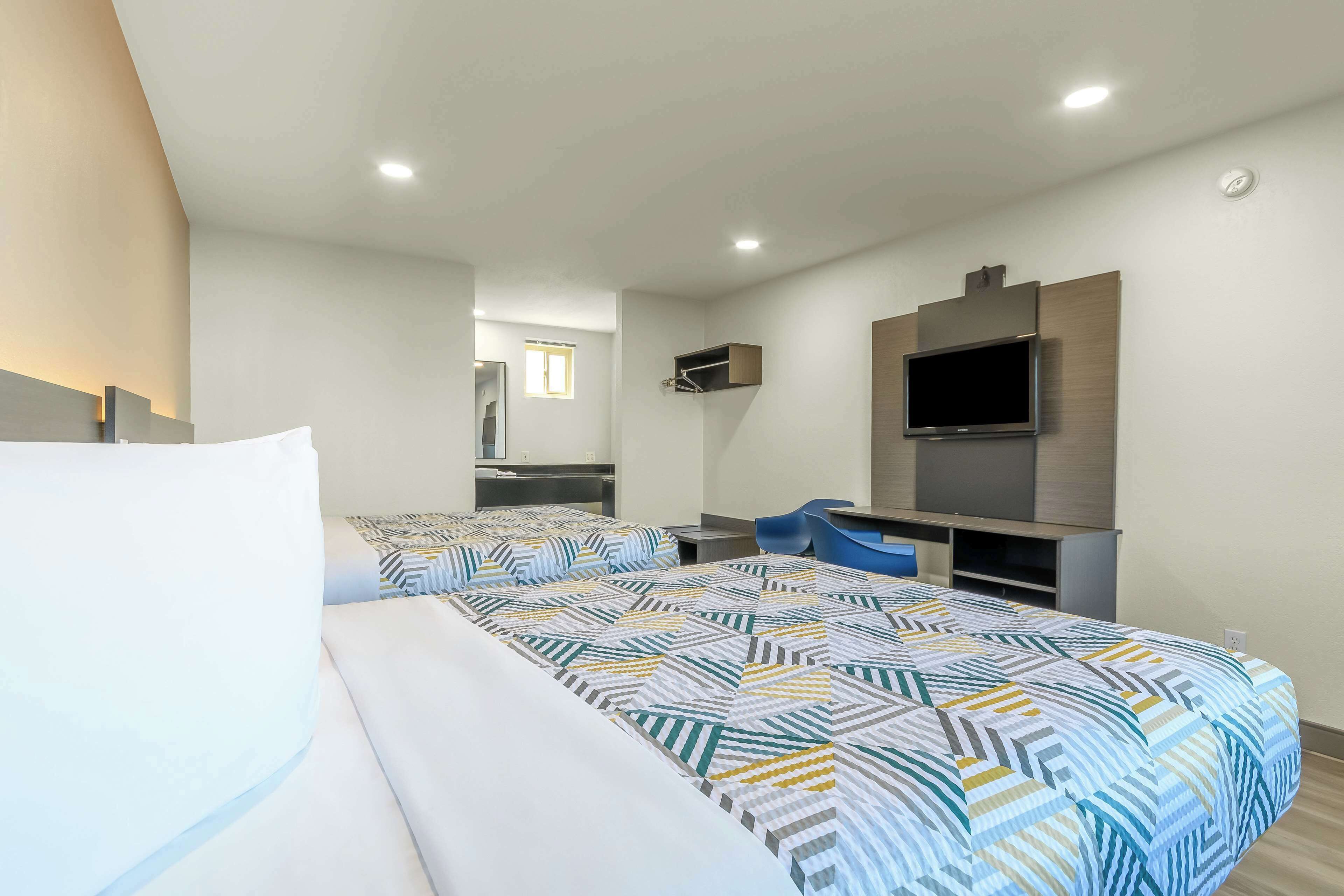 Ein Hotelzimmer mit Bett, Schreibtisch, Stuhl, Fernseher und einer Küchenzeile.