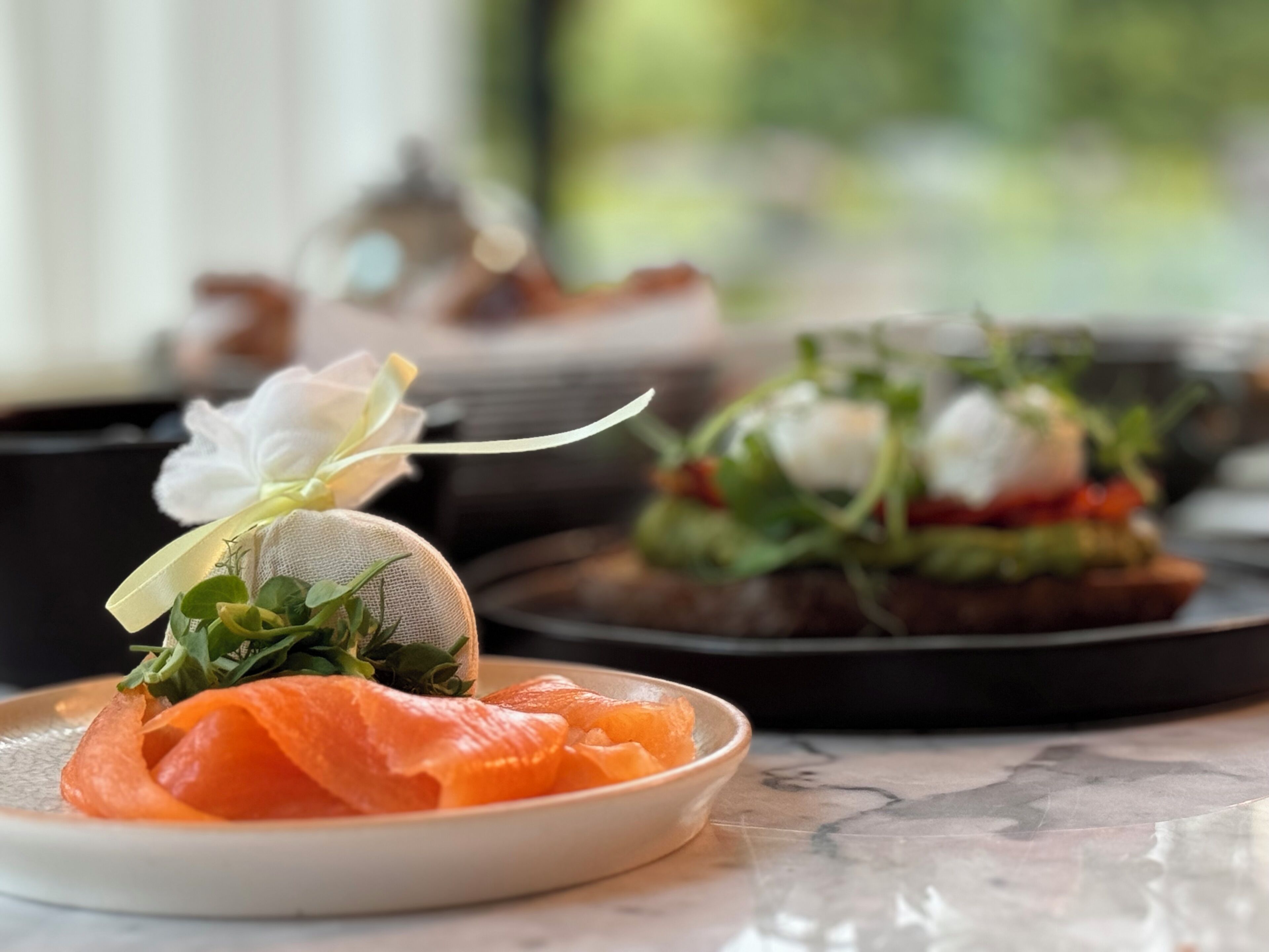 A plate of smoked salmon with a decorative flower on a marble table.