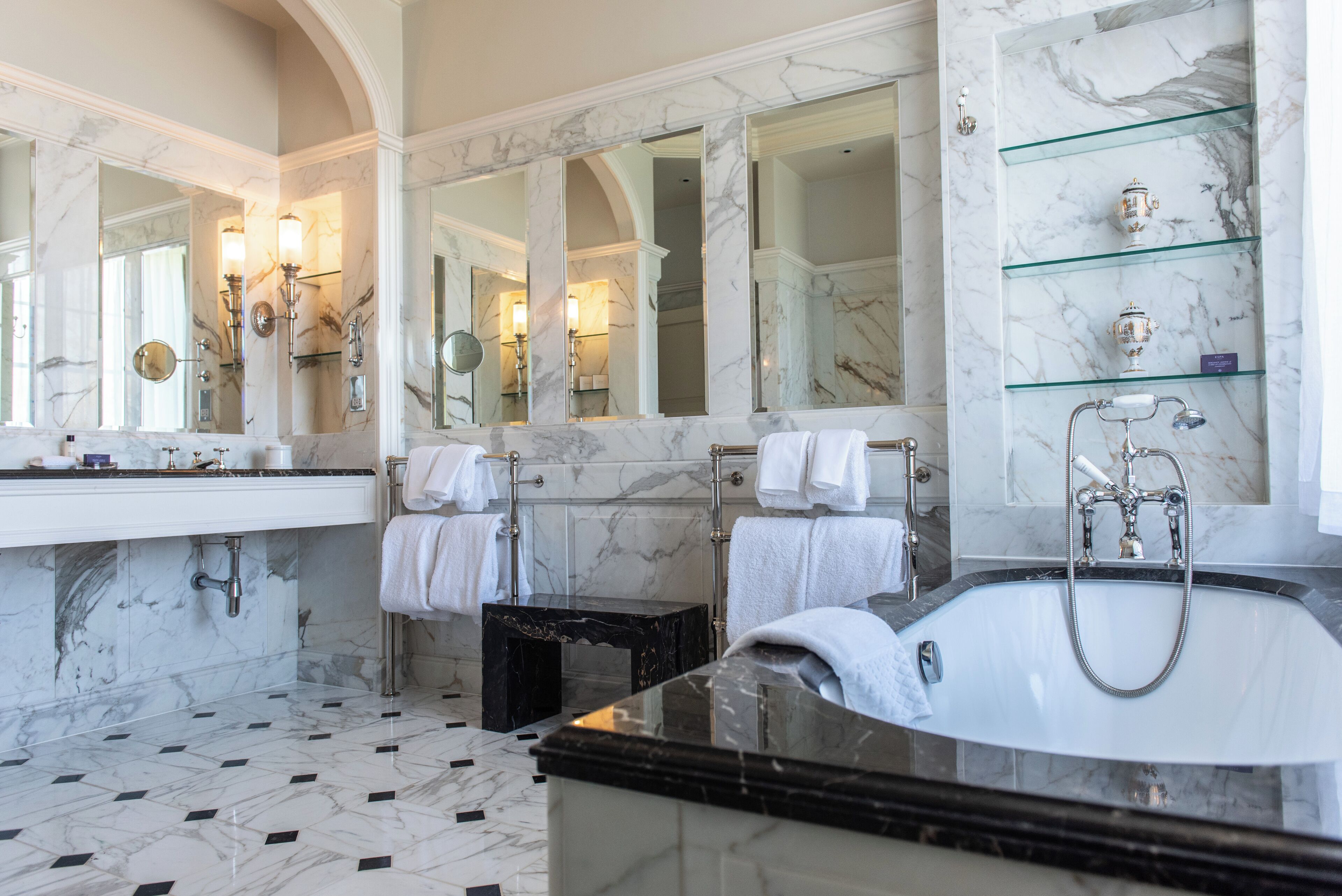 A luxurious bathroom with a large marble sink, a freestanding bathtub, and multiple mirrors.