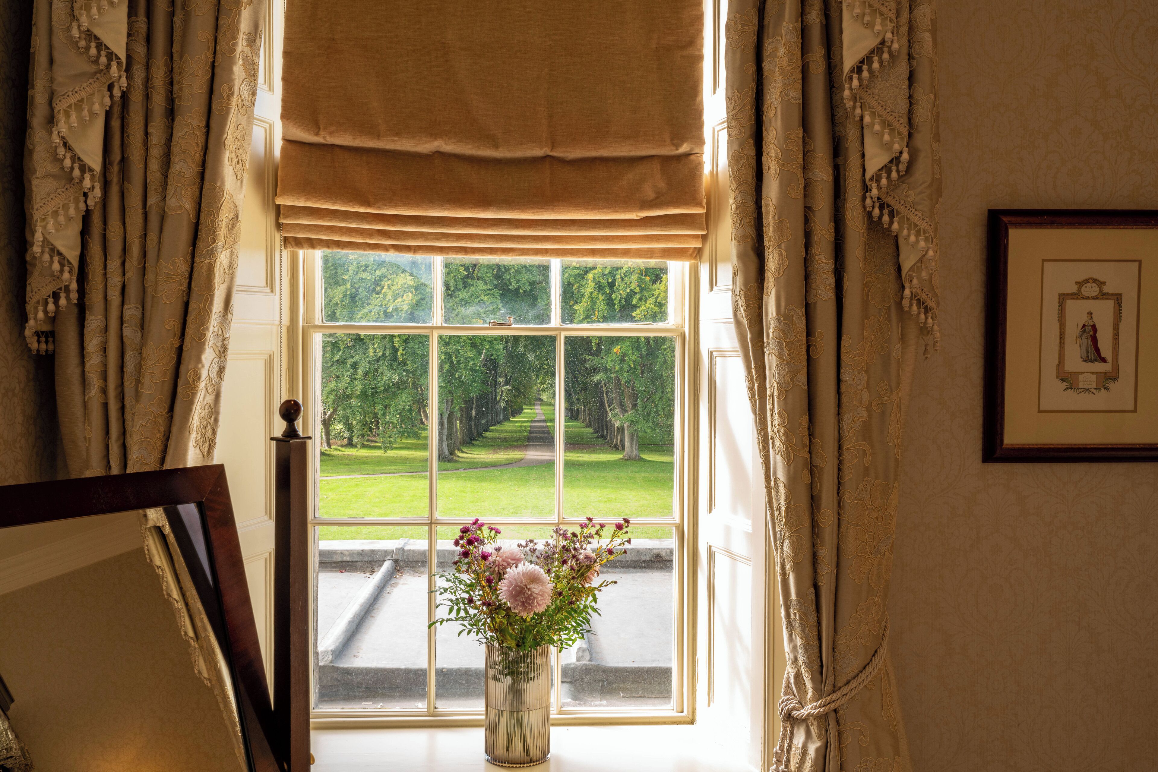 A window with a view of a manicured garden and a framed picture on the wall.