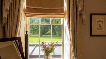 A window with a view of a manicured garden and a framed picture on the wall.