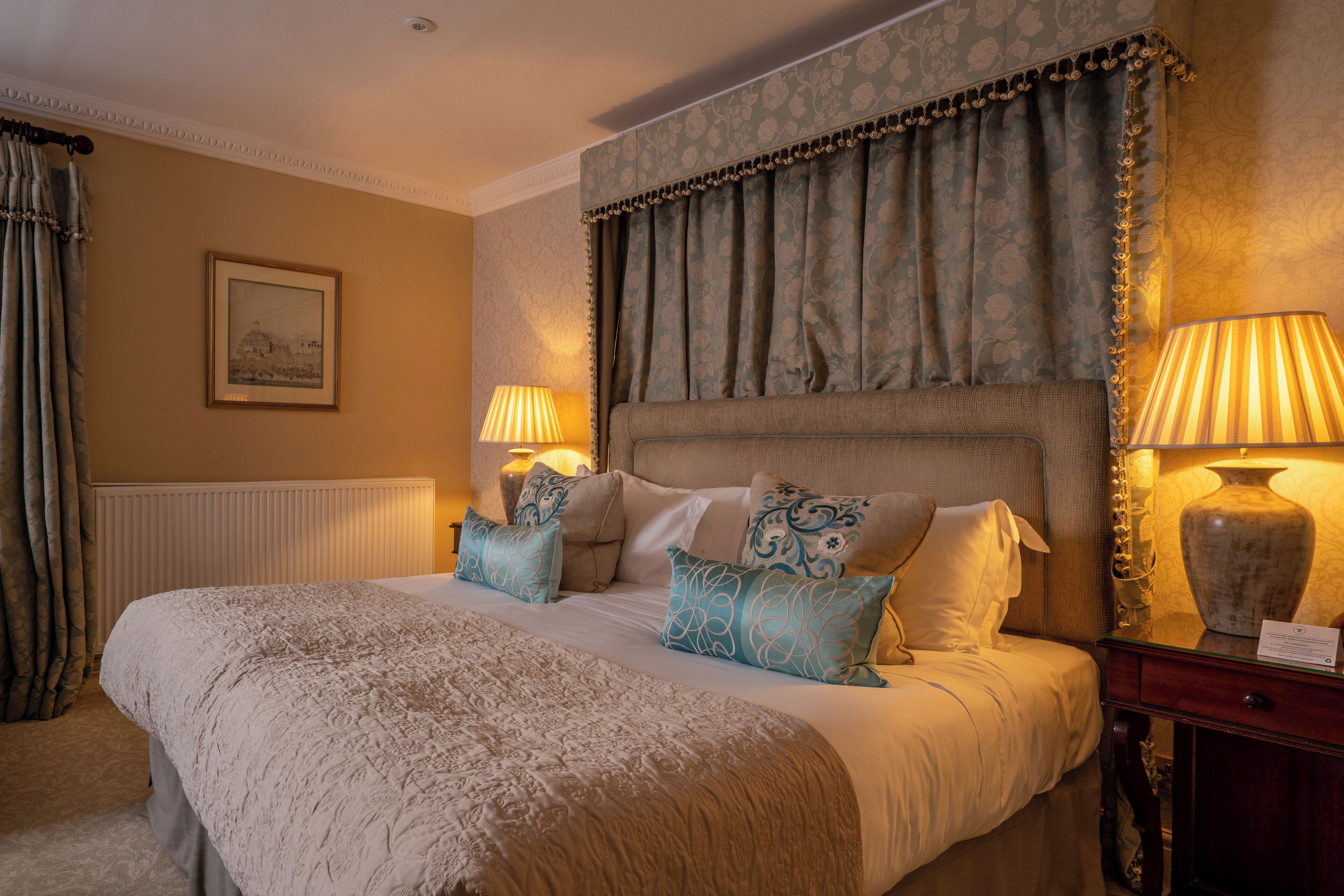 Habitación de hotel elegante con una cama grande, dos lámparas de noche, un jarrón y un cuadro en la pared.