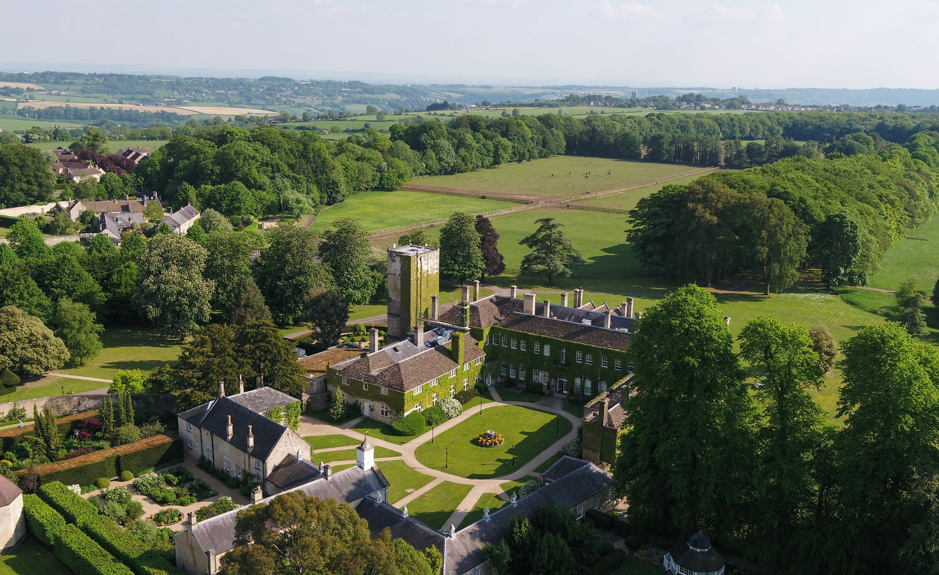 An aerial view of a historic estate with a large manor house, formal gardens, and expansive green fields.