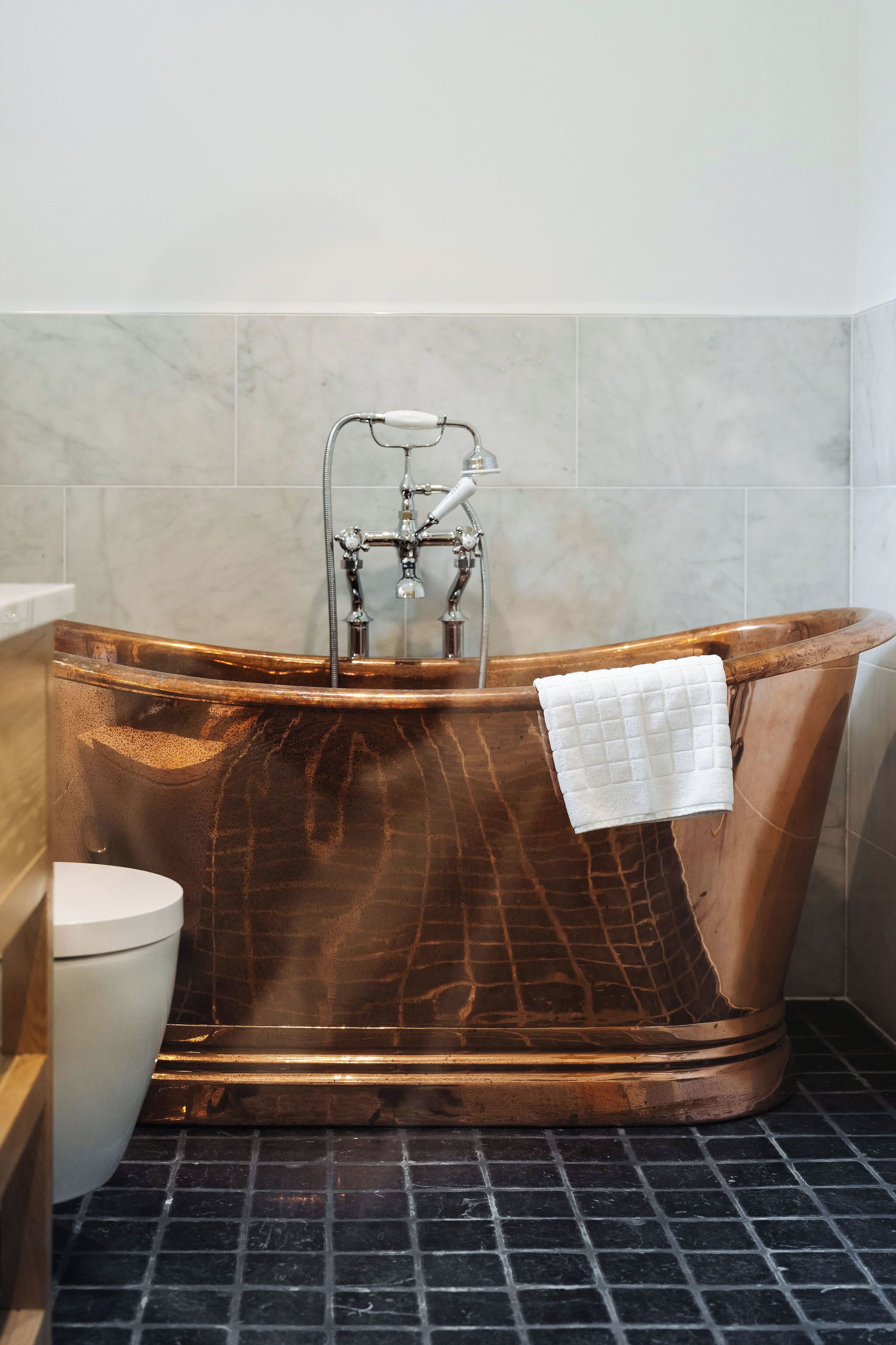 A bathroom with a copper bathtub, a white toilet, and a showerhead.