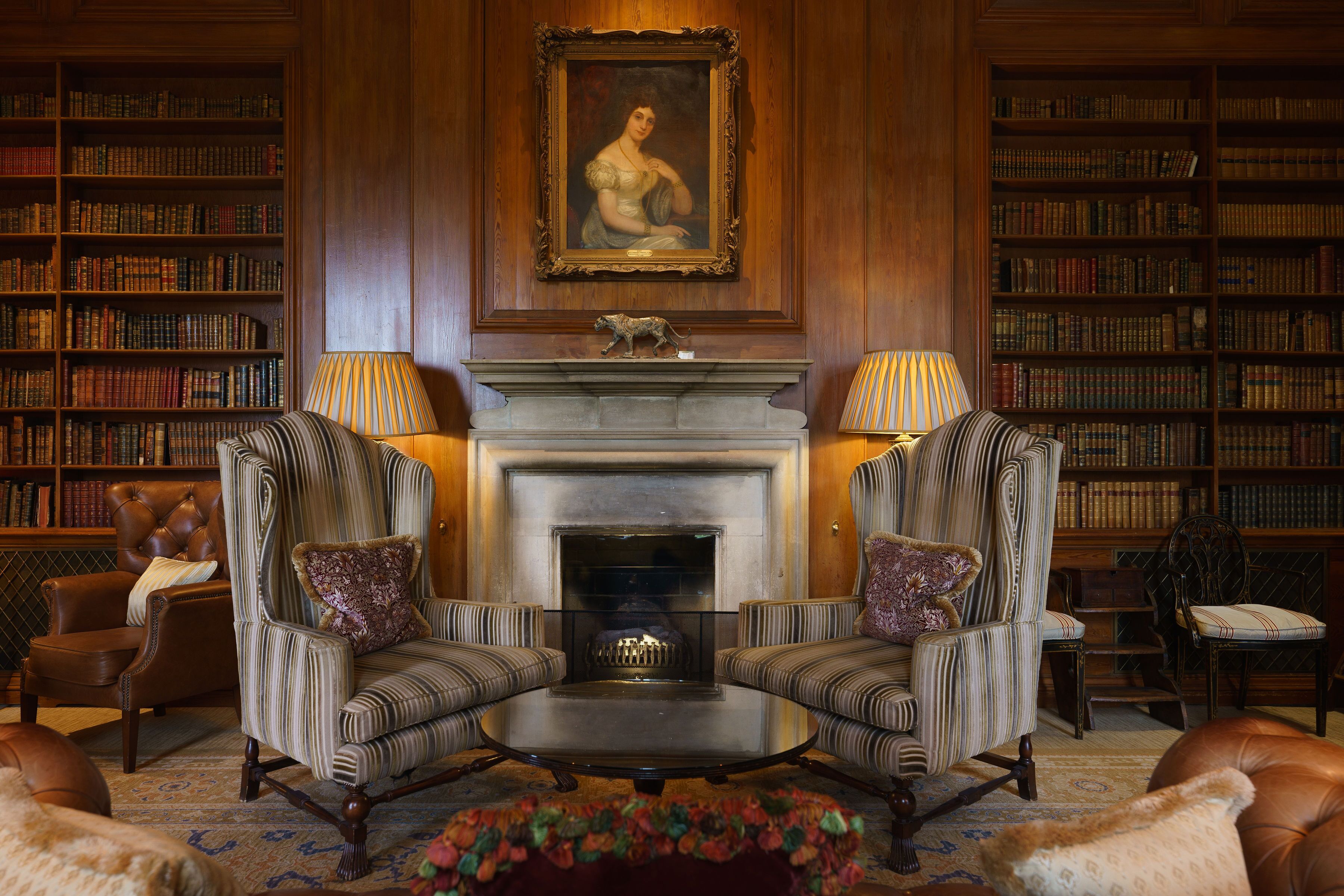A library with leather armchairs, a fireplace, and bookshelves filled with books.