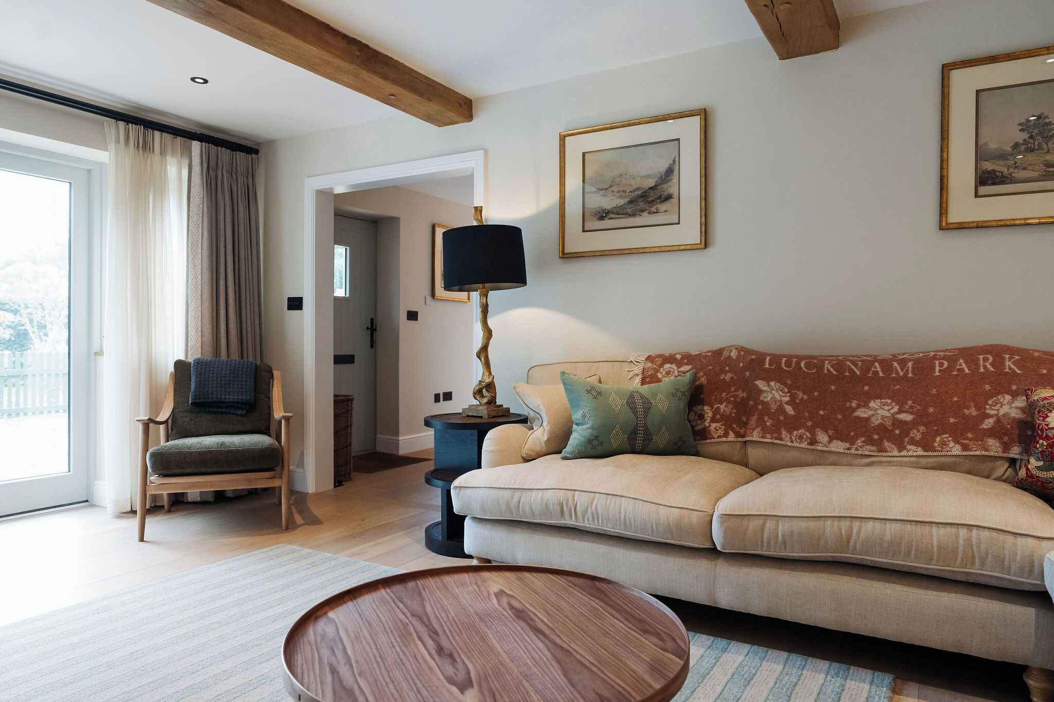 Un salon confortable avec un canapé, un fauteuil, une lampe et une vue sur une porte donnant sur une autre pièce.