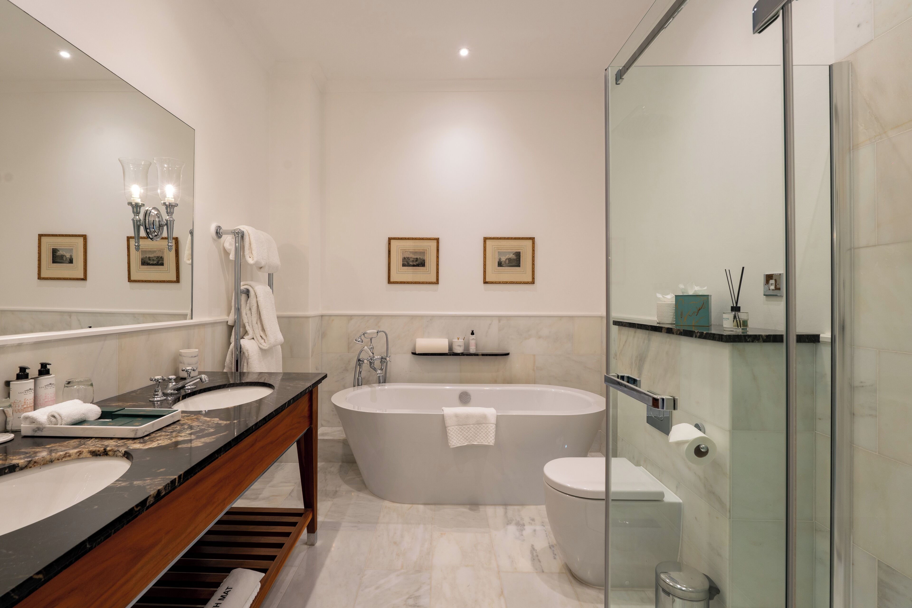 Un baño moderno con una bañera independiente, un inodoro separado, una ducha con mampara de vidrio y un tocador con encimera de mármol.
