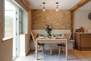 Un comedor con pared de piedra, vigas de madera y una mesa preparada para dos personas con sillas.