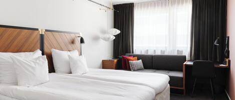 A hotel room with a large bed, a desk, a chair, a sofa, and a window with curtains.