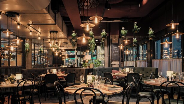 A restaurant with round tables, black chairs, hanging pendant lights, and large windows. - Clarion Hotel Amaranten (Stockholm)