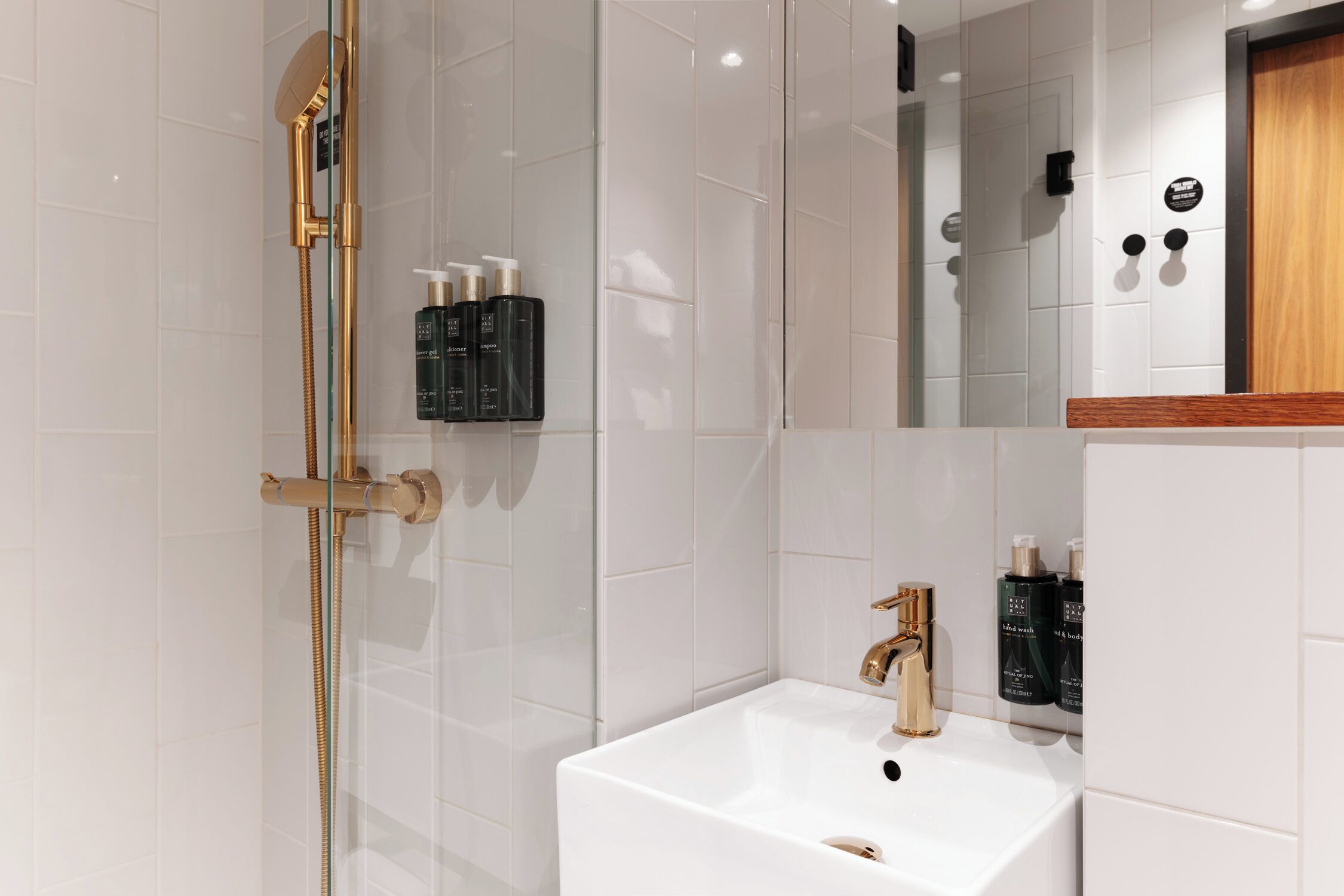 A modern bathroom with a white sink, gold fixtures, and a glass shower enclosure.