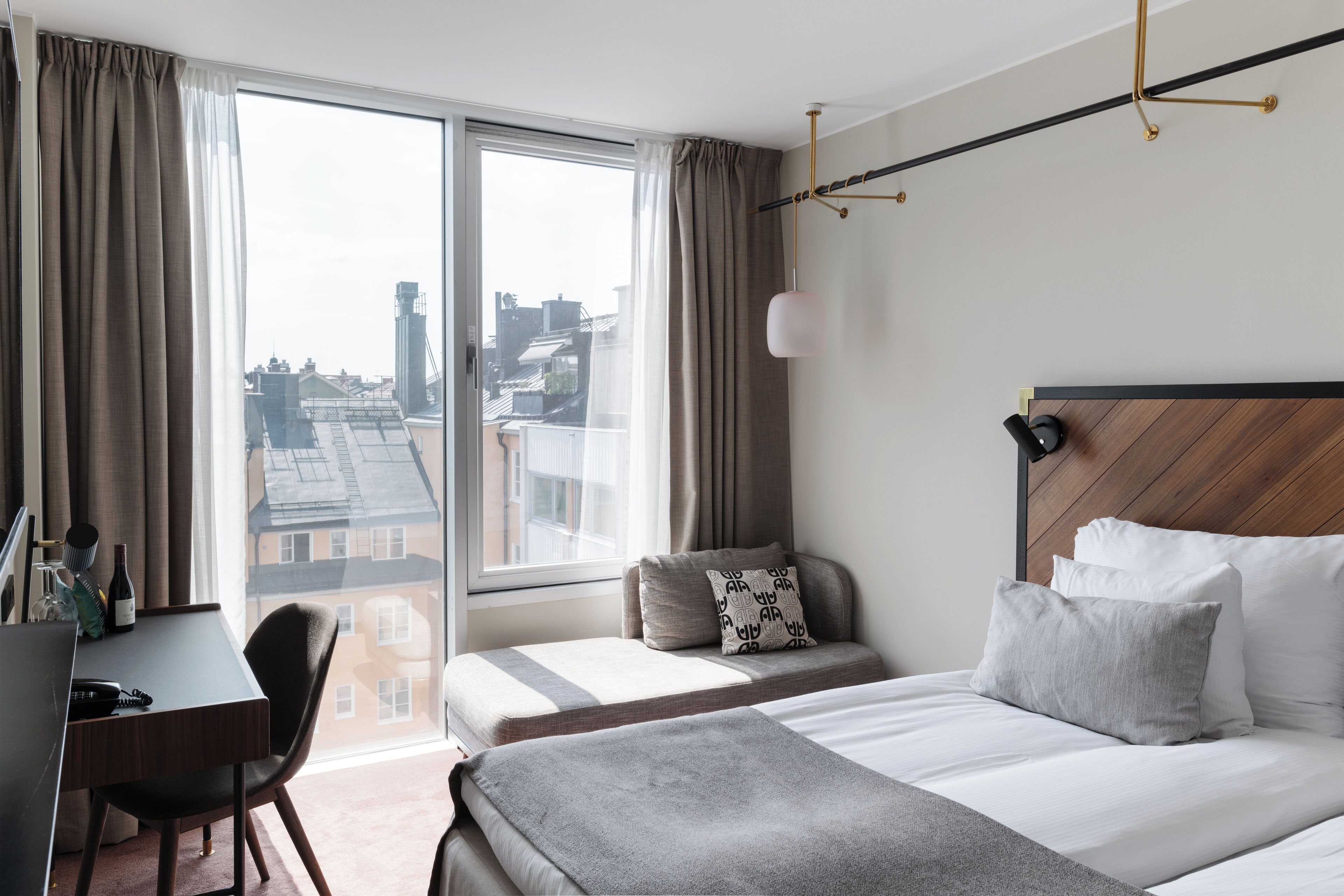 Une chambre d’hôtel avec une grande fenêtre, un bureau, deux lits et une vue sur le paysage urbain.