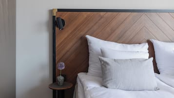A neatly made bed with white linens and two pillows, a small round table with a vase of flowers, and a wooden headboard with a chevron pattern.