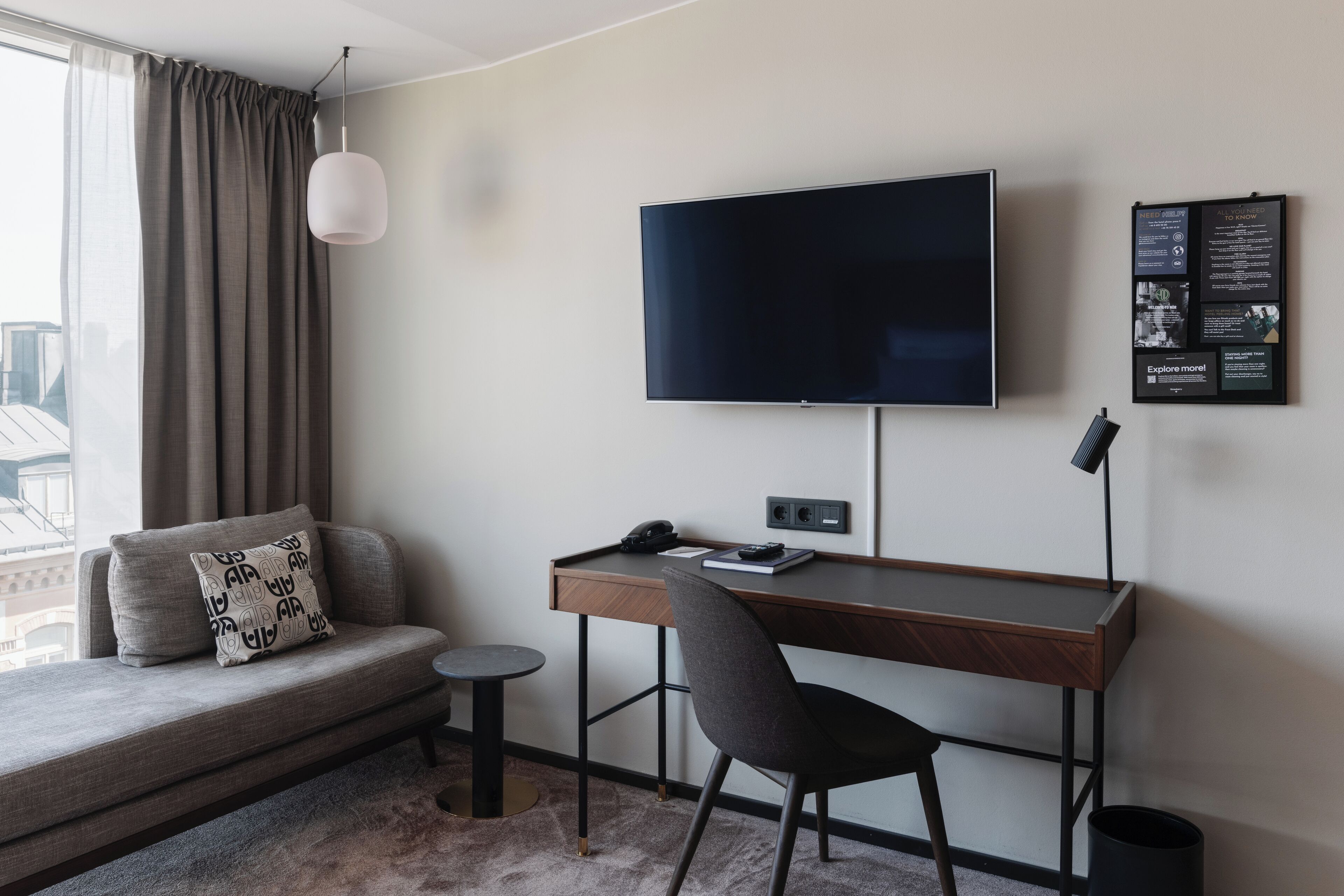 Una camera d'albergo moderna con divano, scrivania, sedia, televisore e un piccolo tavolo.
