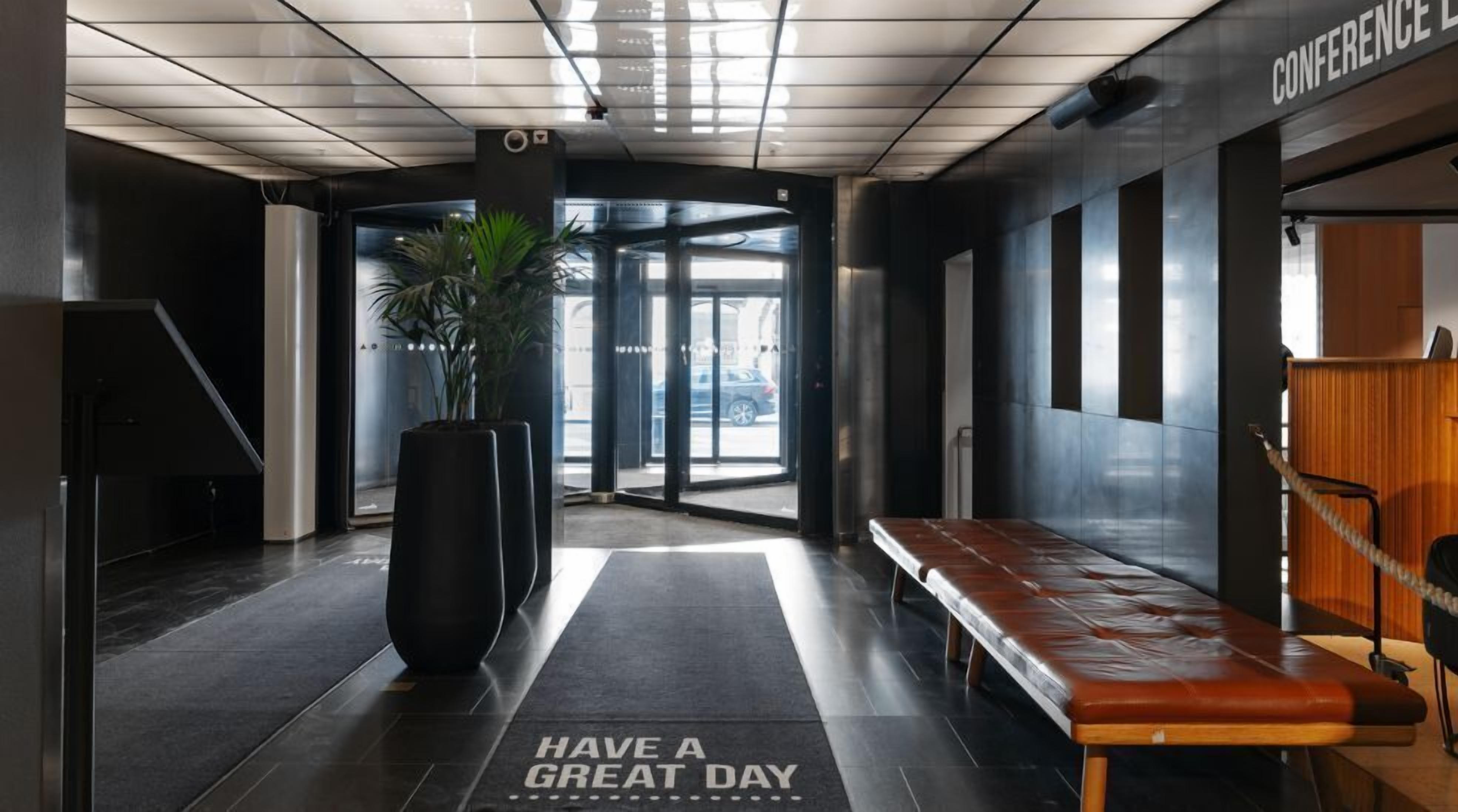Eine moderne Lobby mit einer Bank, einer Fußmatte mit dem Aufdruck 'Have a great day' und einem Konferenzbereich.