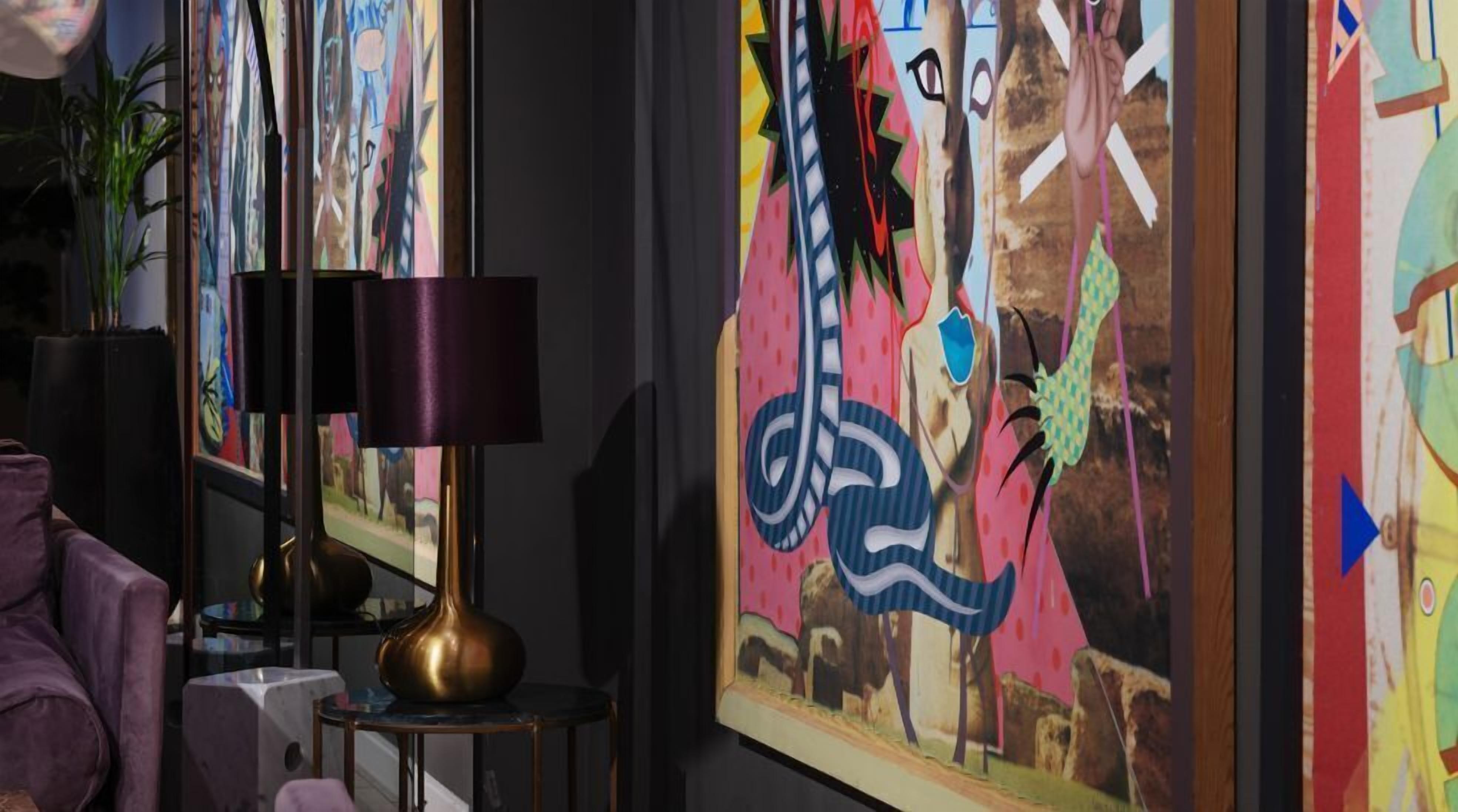 Una habitación con una lámpara moderna, un sillón morado y pinturas abstractas de colores en la pared.