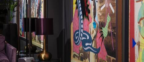 Una habitación con una lámpara moderna, un sillón morado y pinturas abstractas de colores en la pared.
