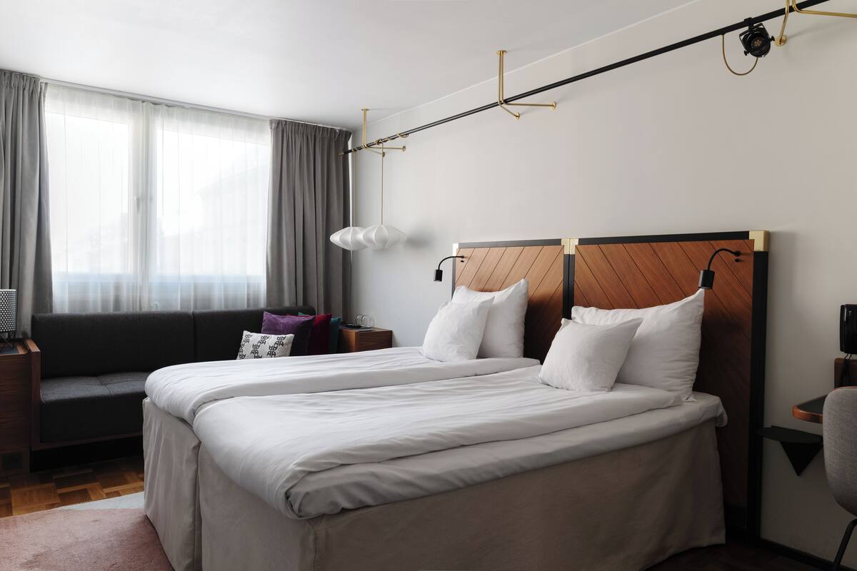 Quarto de hotel moderno com uma cama grande, um sofá, uma escrivaninha e uma janela com cortinas.