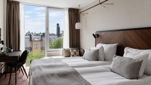 A hotel room with a large window, a desk, and a bed with multiple pillows. - Clarion Hotel Amaranten (Stockholm)