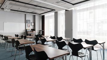 A classroom with desks and chairs arranged in rows, a whiteboard, and large windows with sheer curtains.