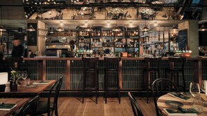 A bar area with wooden bar counters, multiple hanging pendant lights, and shelves stocked with bottles. - Clarion Hotel Amaranten (Stockholm)