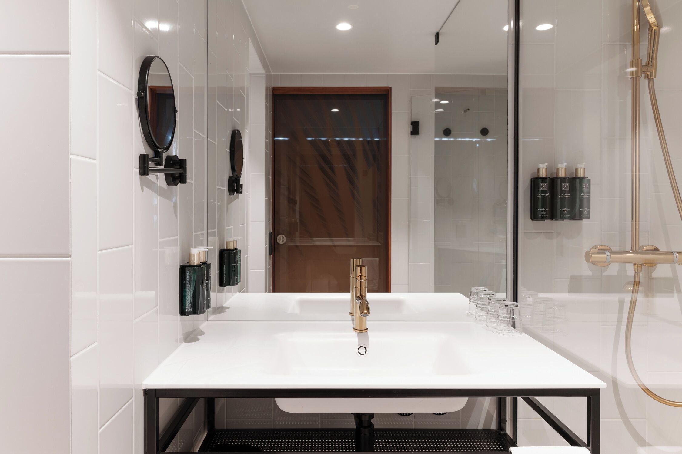 A modern bathroom with a white sink, gold faucet, and a glass shower enclosure.