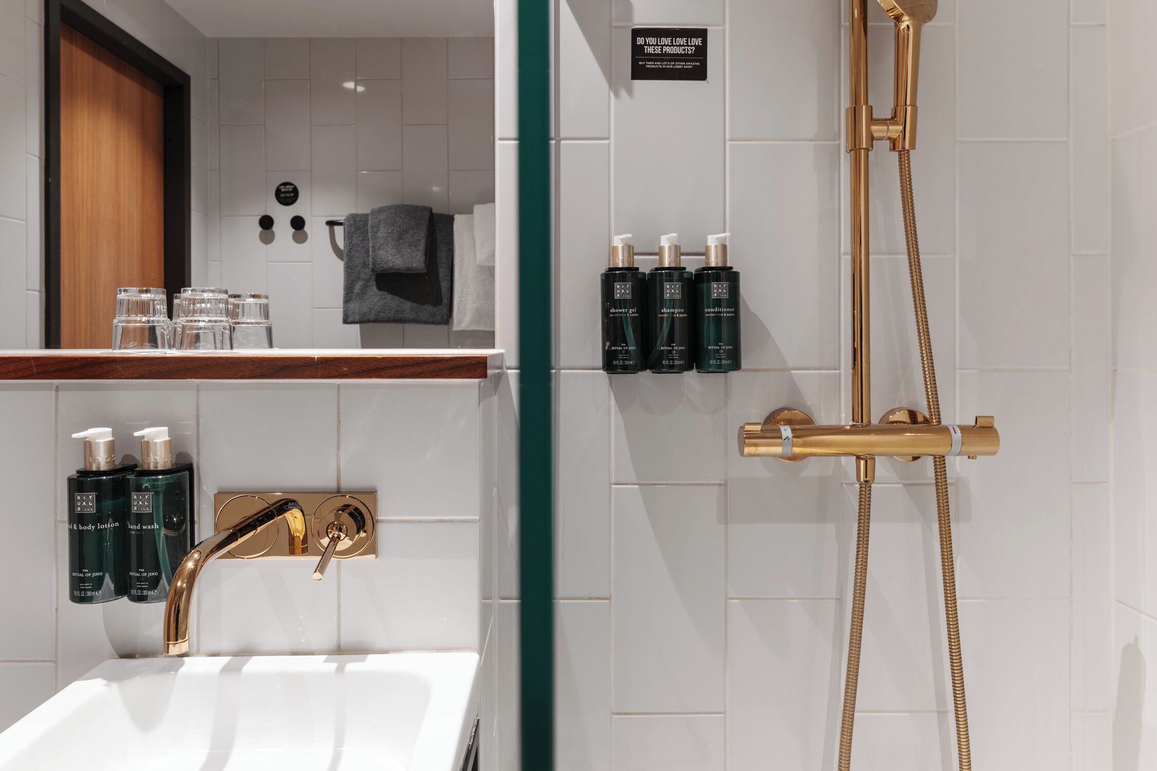 A modern bathroom with a gold faucet, a shower with a gold hose, and toiletries on the wall.