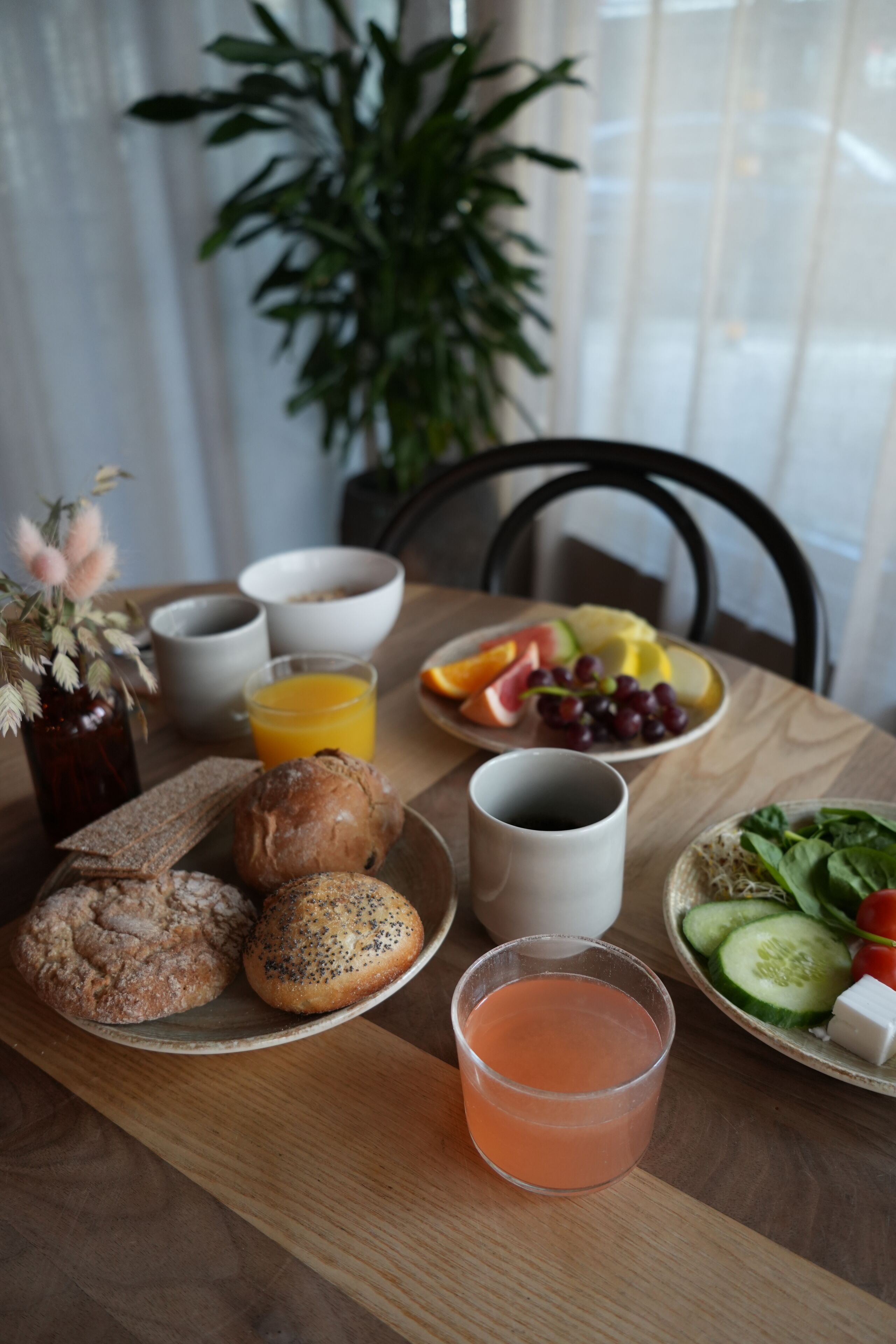 A breakfast table with bread, pastries, fruit, and a drink.
