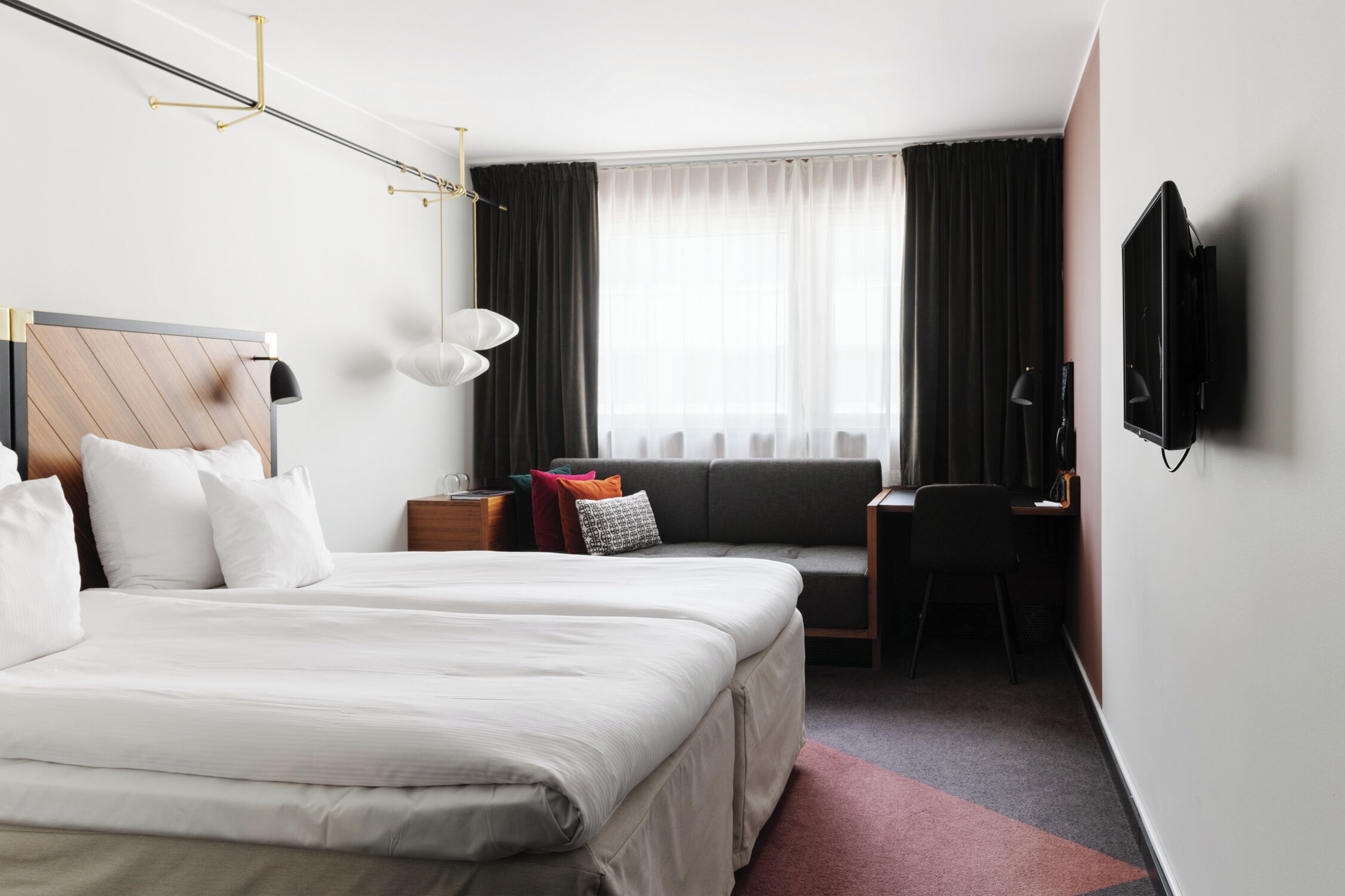 Habitación de hotel con una cama grande, un escritorio, una silla, un televisor y un ventanal con cortinas.