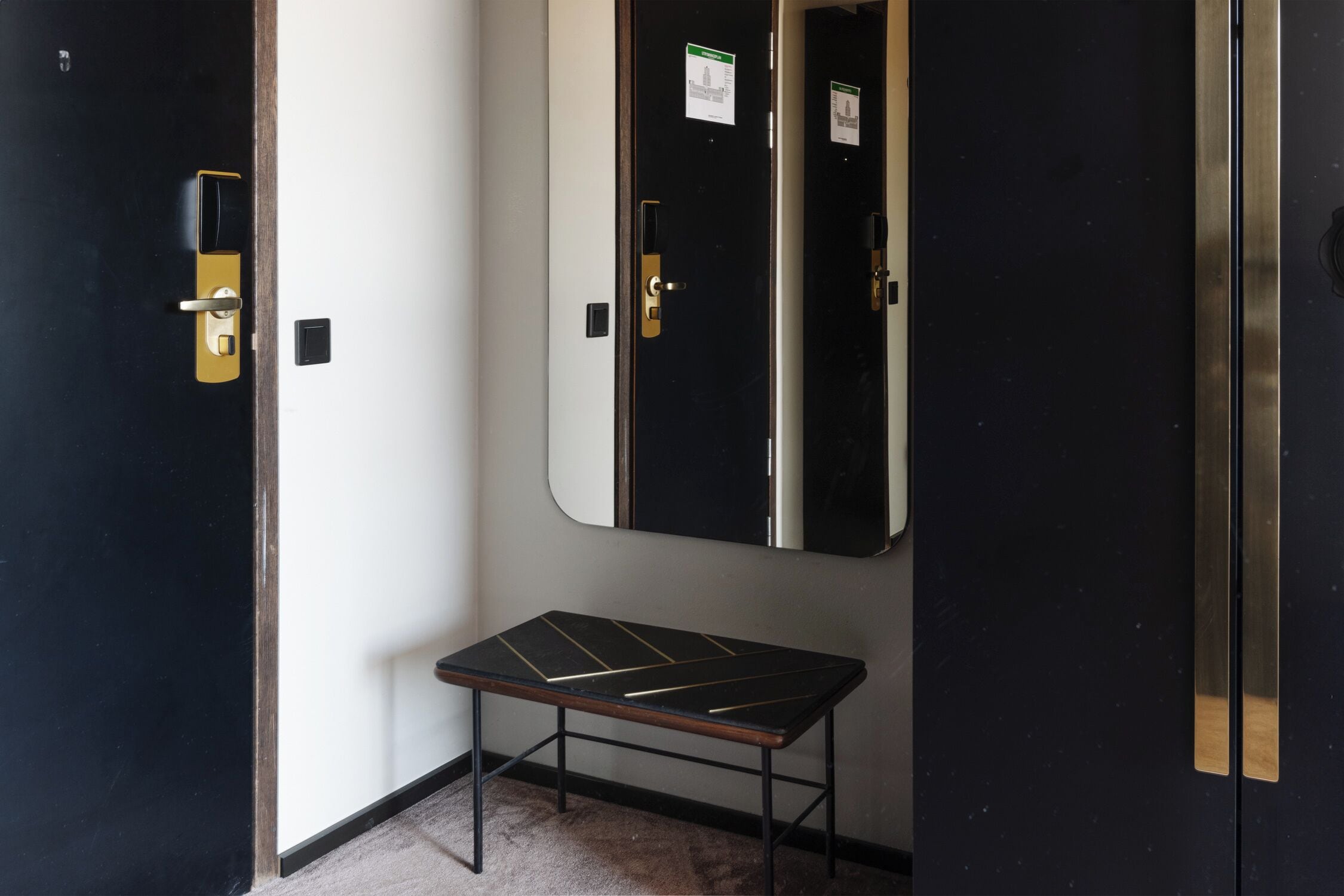 Una habitación con una puerta negra, una mesita y un espejo en la pared.