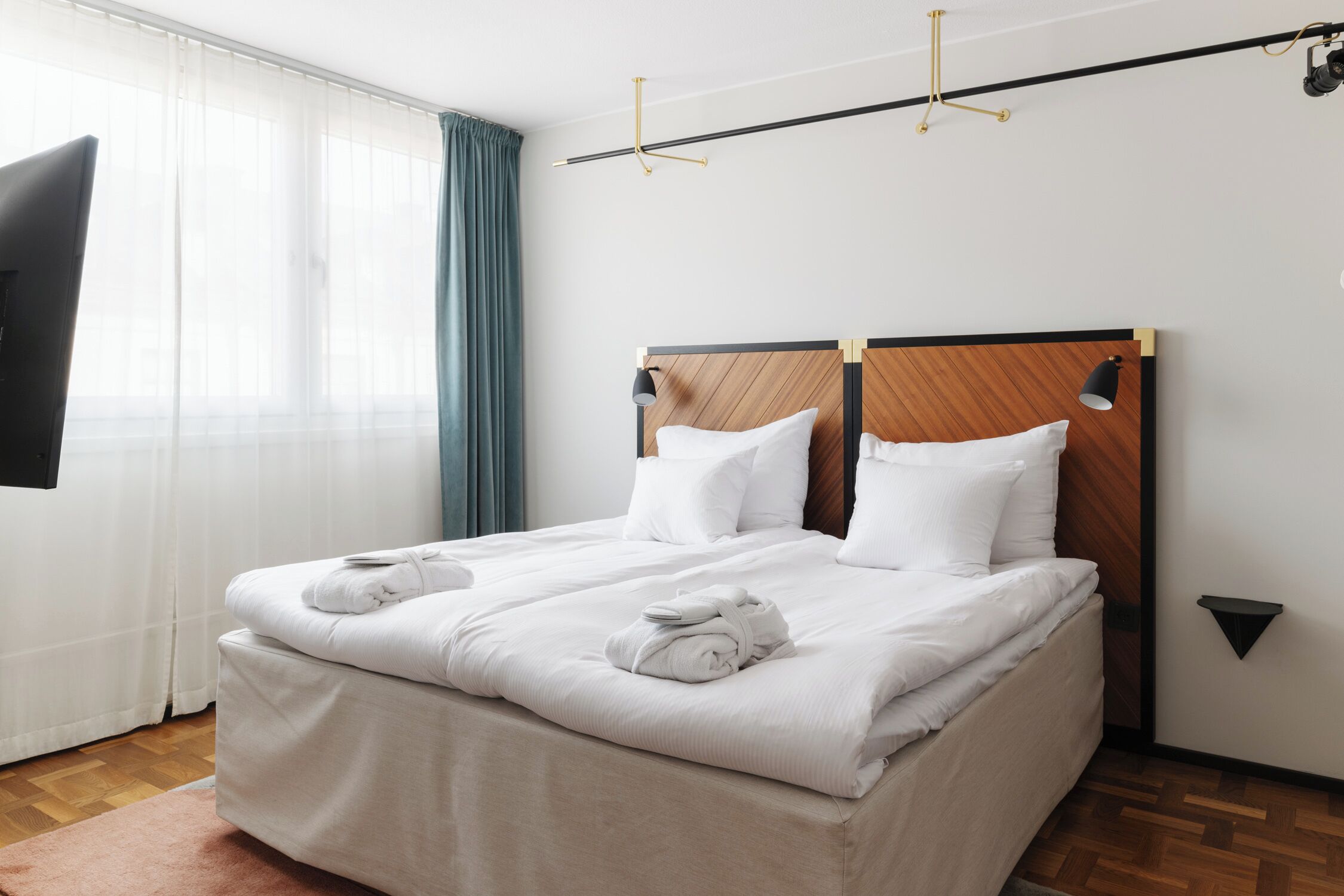 A neatly made bed with white linens and towels, a wooden headboard, and a small black nightstand with a lamp.