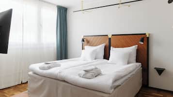 Una cama bien hecha con sábanas y toallas blancas, un cabecero de madera y una mesita de noche negra con una lámpara.