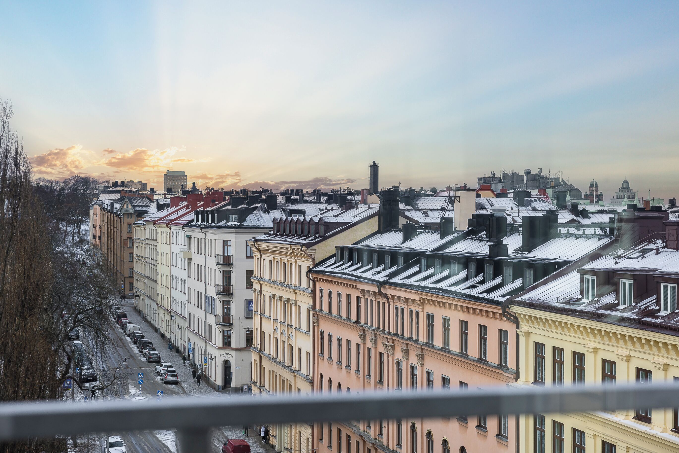 Une vue urbaine avec des immeubles à plusieurs étages, un ciel dégagé et une rue bordée de voitures garées.