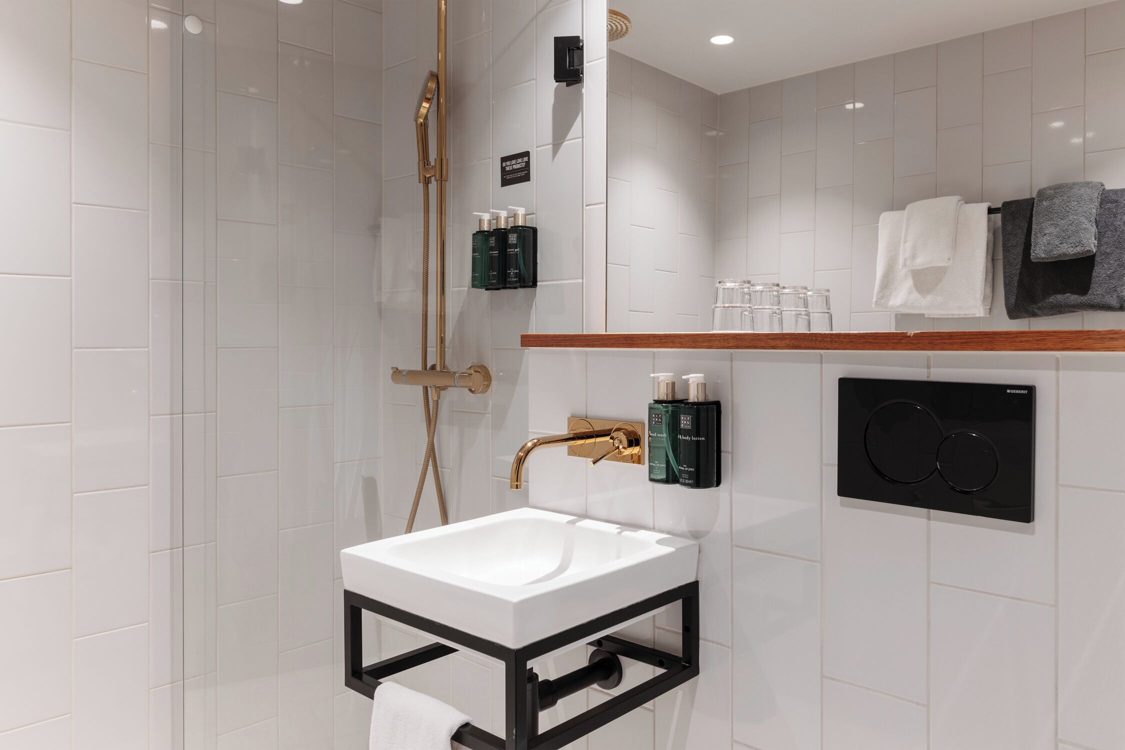 A modern bathroom with a white sink, gold fixtures, and a black towel rack.