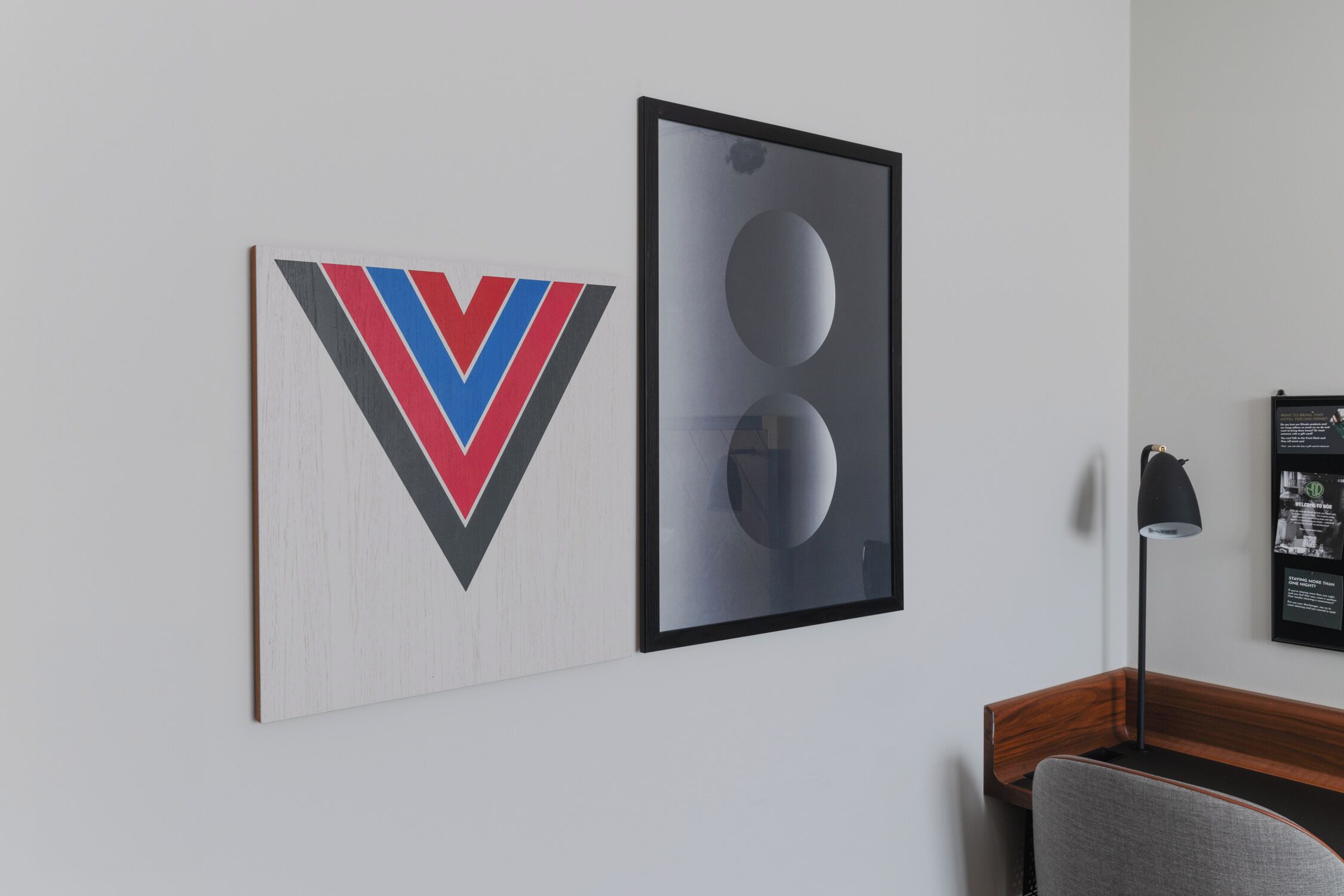 A room with a modern design, featuring a wooden desk and a chair, a framed artwork on the wall, and a floor lamp.