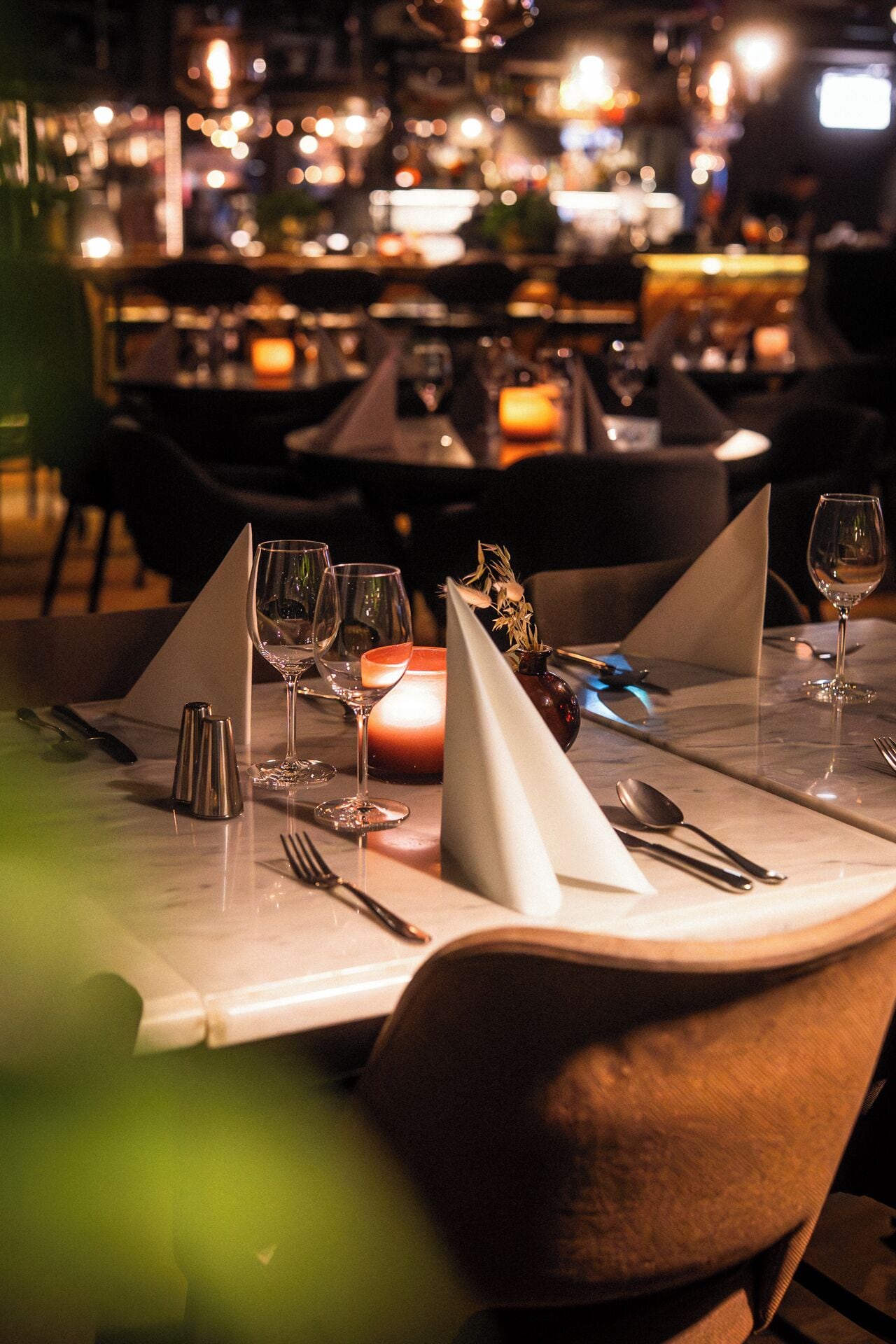 A restaurant setting with tables set for dining, featuring candles and glassware.