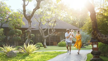 Un chemin aménagé dans un jardin bien entretenu, bordé d’arbres et d’arbustes, qui mène à un bâtiment doté d’un toit en tuiles.